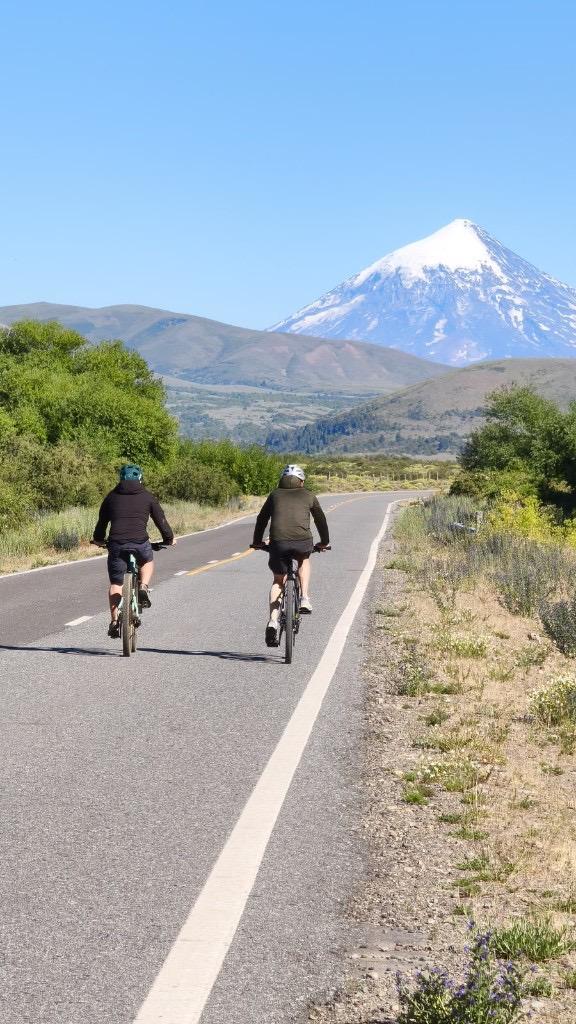 Ciclistas en una ruta de Patagonia con un volcán nevado al fondo