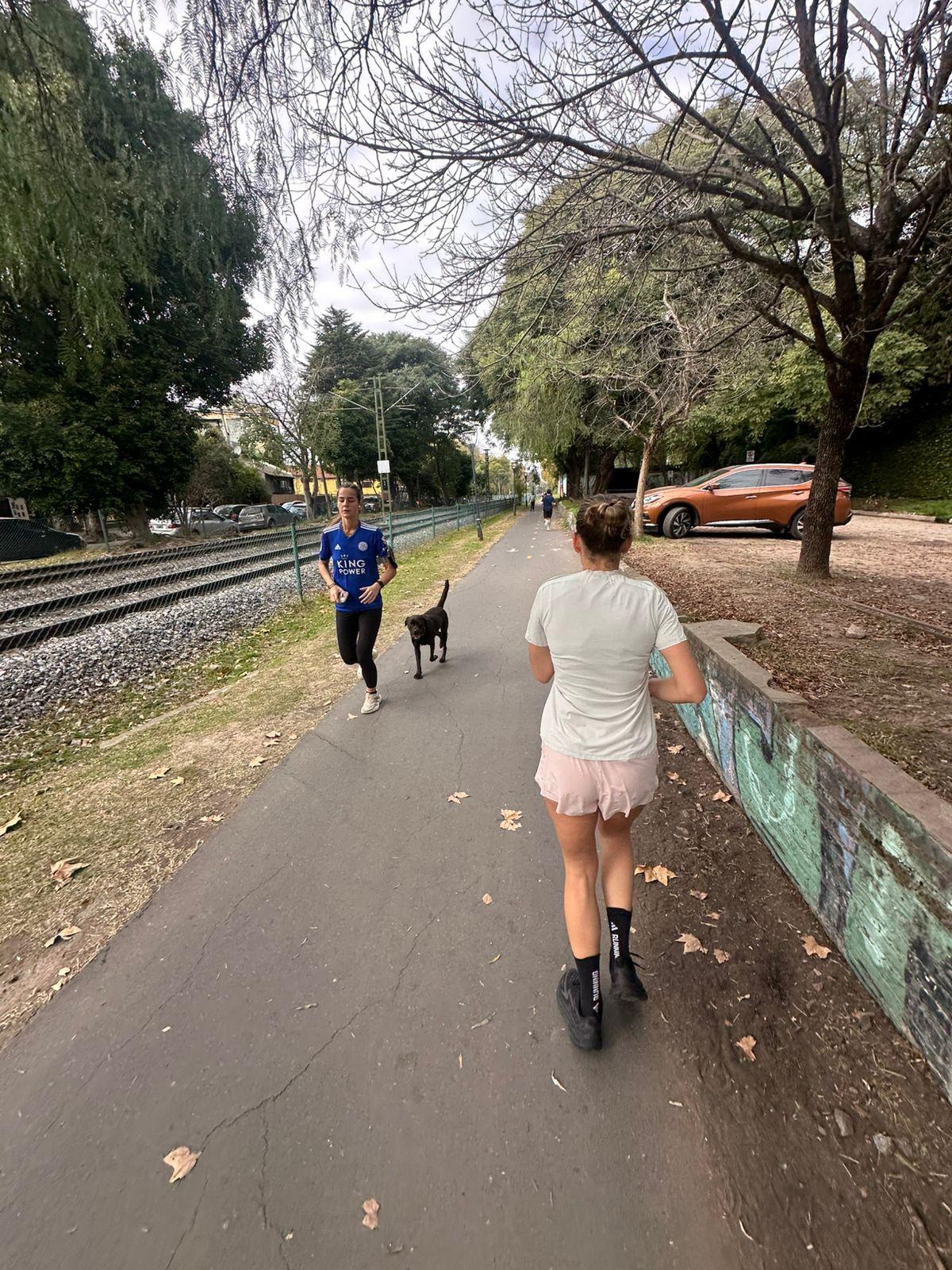 Corredoras cruzándose en el corredor de San Isidro, con un perro en ruta